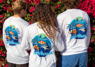 Three people standing with the backs to the camera wearing white long-sleeved exercise shirts.